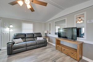 A living room with a leather sofa, wooden entertainment unit, ceiling fan, and a large flat-screen TV.
