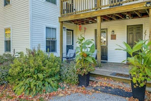 A two-story building with a porch, a door with a sign, and a small garden area with plants and fallen leaves. - Saint Albans Home: Walk to Main Street! (St. Albans)