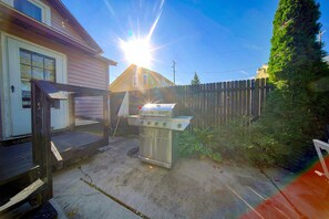 Un jardin avec un barbecue, une terrasse en bois et une maison.