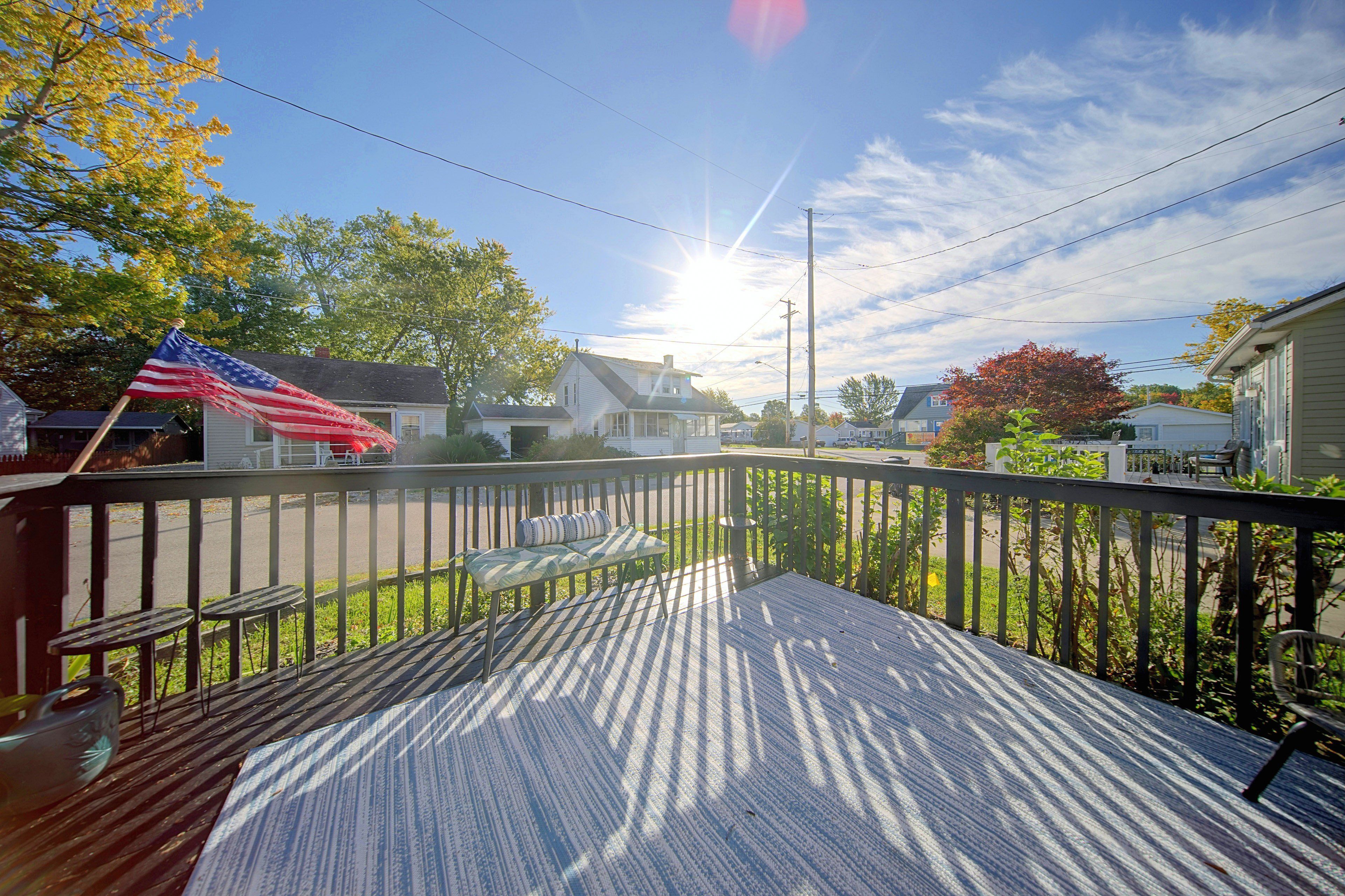 A wooden deck with a view of a residential street, a flag, and houses.