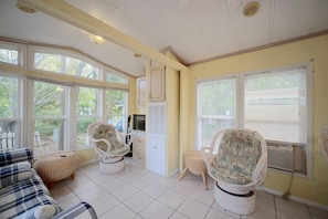 A sunroom with large windows, wicker furniture, and a television. - Water Views + Patio Brews! Middle Bass Island Home (Put-in-Bay)