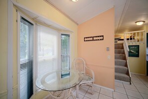 A dining area with a glass table and white chairs, a staircase, and a framed picture on the wall. - Water Views + Patio Brews! Middle Bass Island Home (Put-in-Bay)