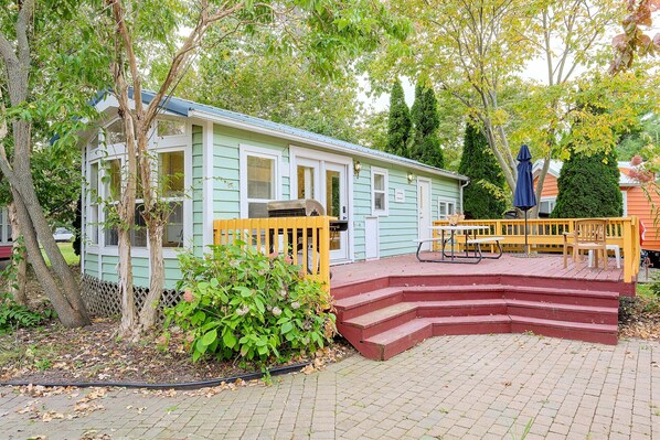 A small, light green house with a porch, a wooden fence, and a picnic table. - Water Views + Patio Brews! Middle Bass Island Home (Put-in-Bay)