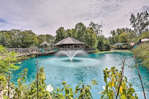 A tranquil outdoor pool with a central fountain, surrounded by lush greenery and a wooden pavilion. - Water Views + Patio Brews! Middle Bass Island Home (Put-in-Bay)