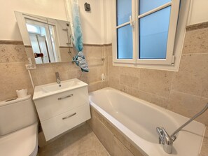 A bathroom with a bathtub, a sink, a mirror, and a window. - New Listing (Paris)