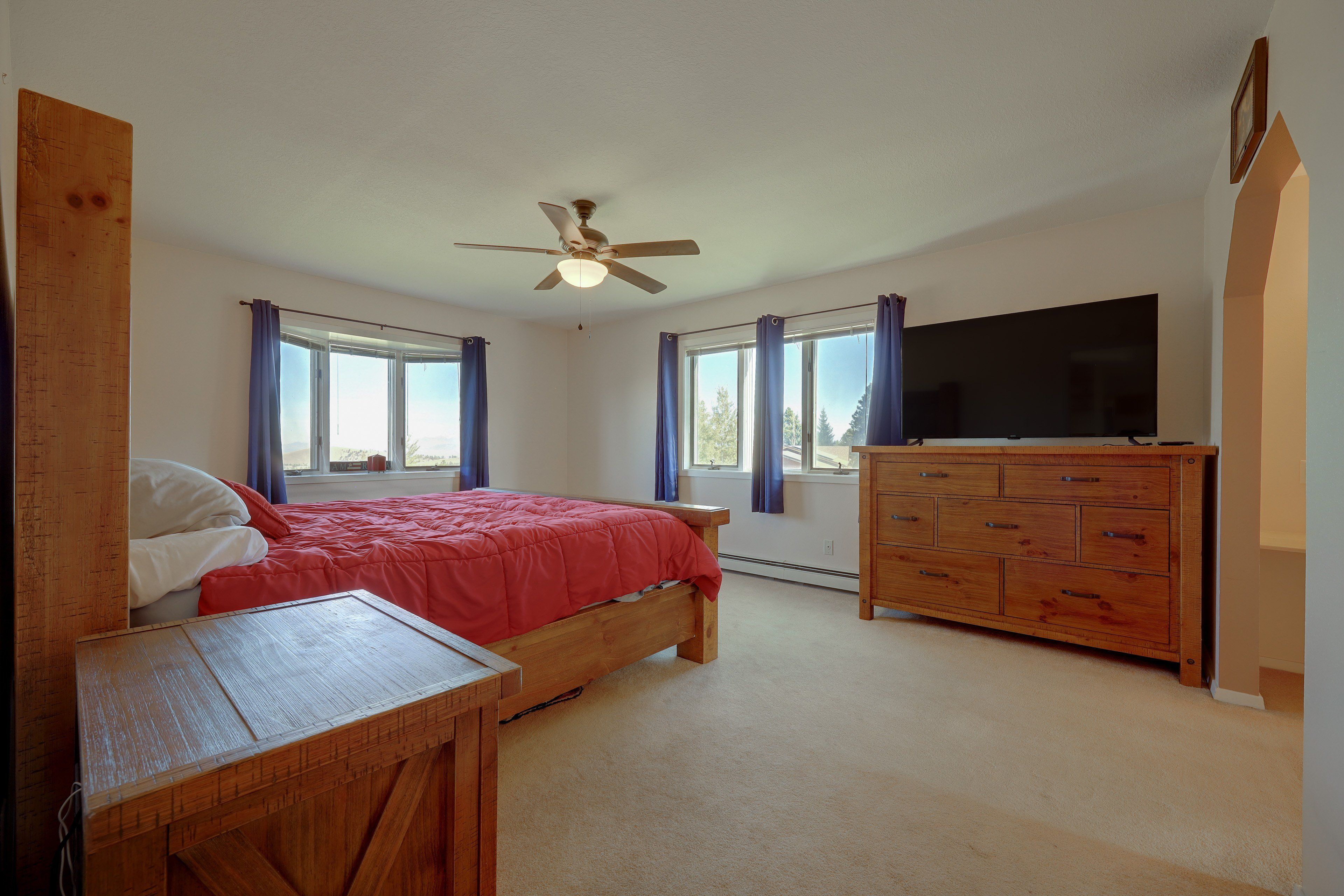 A bedroom with a bed, a wooden dresser, a television, and a ceiling fan.