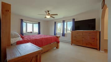 A bedroom with a bed, a wooden dresser, a television, and a ceiling fan.