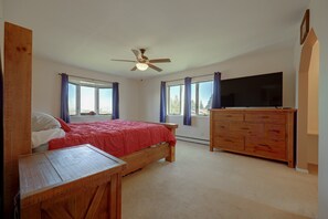 A bedroom with a bed, a wooden dresser, a television, and a ceiling fan.