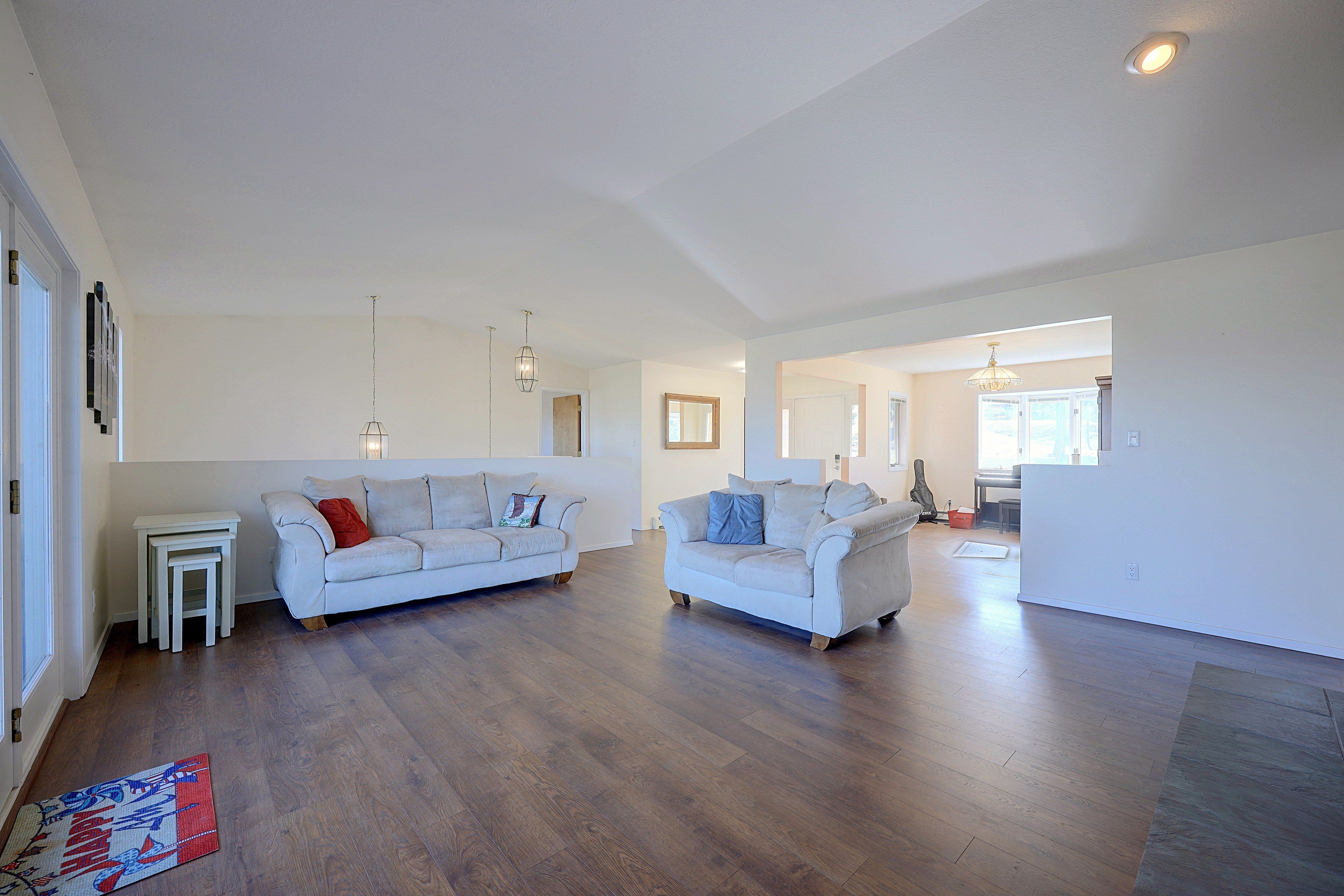 A spacious living area with two sofas, a coffee table, and a small side table. The room has hardwood flooring and white walls.