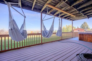 Una terraza de madera con dos hamacas colgadas del techo, una valla de madera y vistas a un paisaje verde.