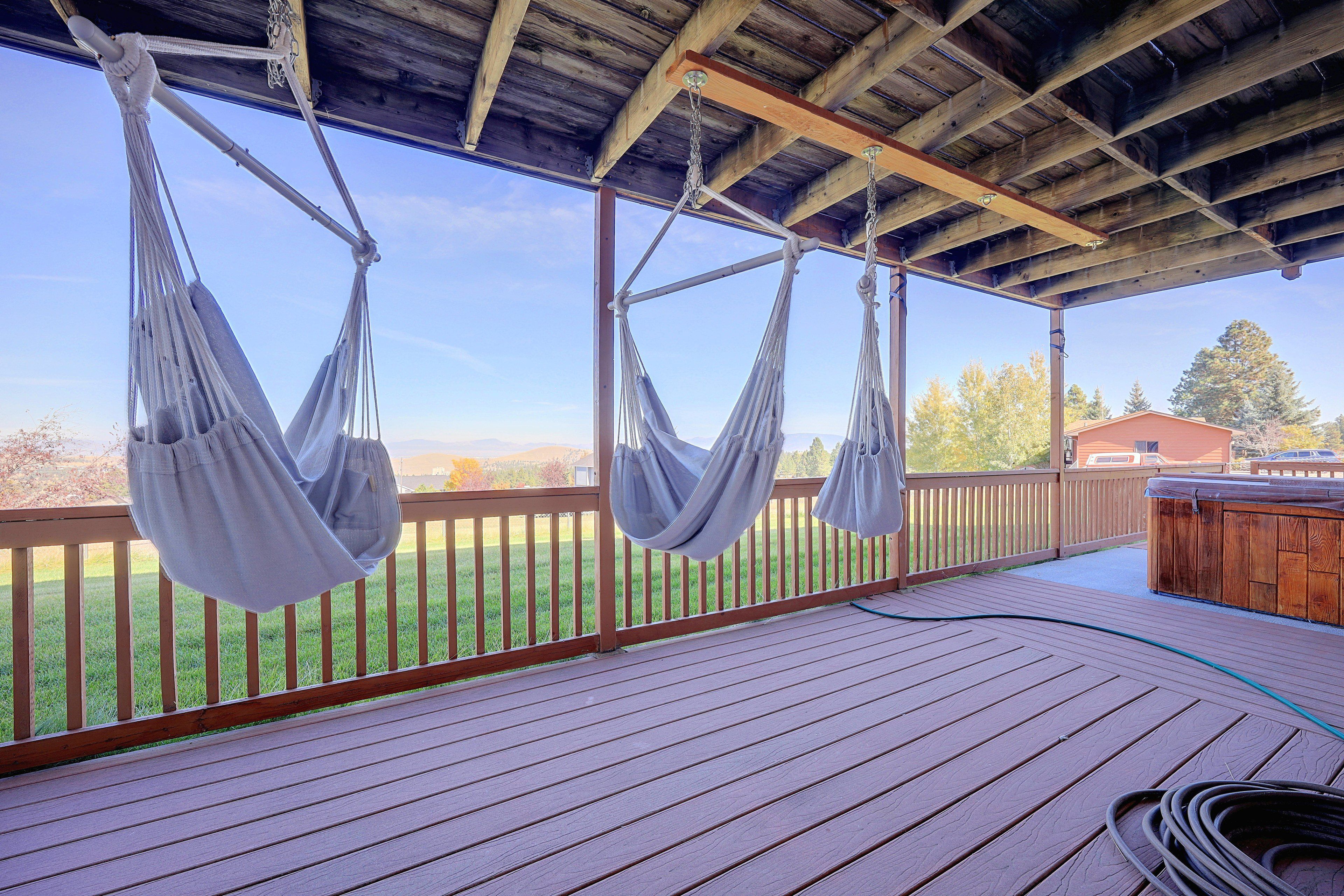 A wooden deck with two hammocks suspended from the ceiling, a wooden fence, and a view of a green landscape.