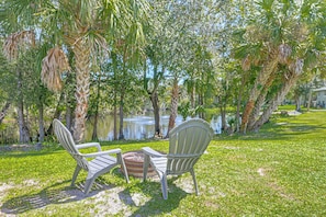 Two chairs facing a pond with trees and a building in the background. - Boathouse Cabin at Horse Creek Retreat (Fort Ogden)