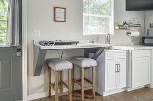 Una cocina con isla integrada, taburetes de bar, microondas y una ventana con persianas.