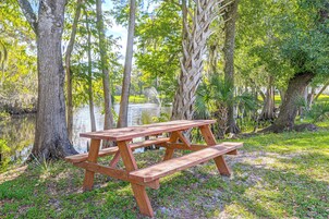 Una mesa de picnic de madera en un entorno natural, con árboles y un cuerpo de agua al fondo.