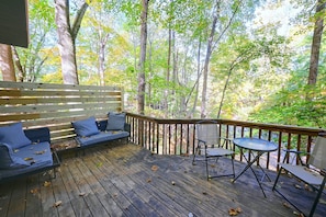 Une terrasse en bois avec un canapé et des fauteuils, entourée d’arbres.