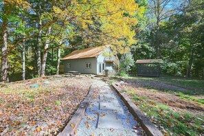 Une cabane rustique avec un toit en métal, entourée d’une forêt aux couleurs automnales.