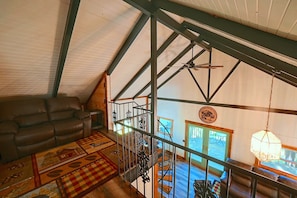 A loft-style room with a high ceiling, exposed beams, a leather sofa, a patterned rug, and a staircase leading to an upper level. - 7 Mi to Hocking Hills! Family & Dog-friendly Haven (Rockbridge)