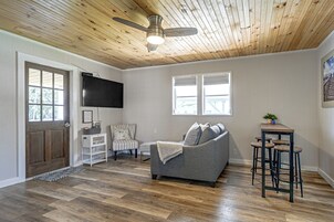 Una sala de estar con un sofá gris, un televisor montado en la pared, un ventilador de techo y suelo de madera.