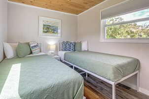 Una habitación con dos camas, una ventana que ofrece vistas a árboles, un cuadro en la pared y una lámpara en la mesita de noche.