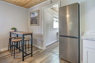 Una cocina con un refrigerador de acero inoxidable, una mesa de madera con taburetes y un cuadro en la pared.