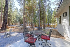 A patio with a round table and chairs, surrounded by trees and a building. - Bring Your Boat! Home w/ Patio Near Lake Almanor (Chester)