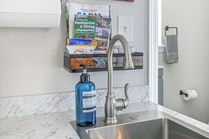 Un lavamanos de cocina con un grifo moderno, un dispensador de jabón para platos y una guía de viaje colgada en la pared.