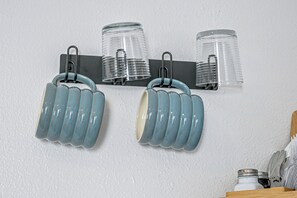 A kitchen with a white wall, a black metal rack holding three clear glass jars, and two blue ceramic mugs hanging from the rack. - Otter Creek Cabin - Horse Creek Retreat Arcadia (Fort Ogden)
