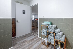 Baño de hotel con suelo de madera, un perchero con toallas enrolladas ordenadamente y un letrero que indica un aseo.