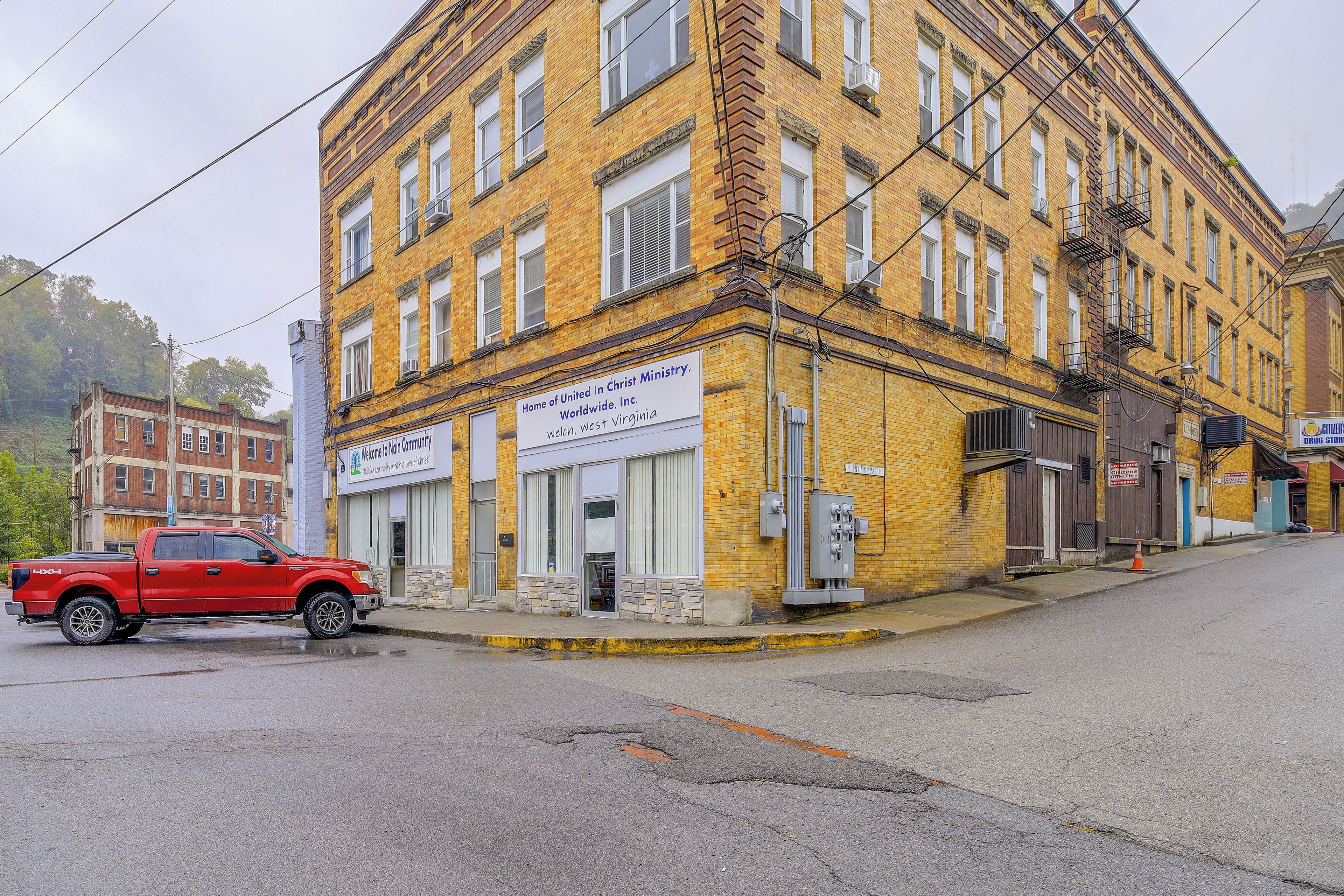 A multi-story yellow brick building with a red pickup truck parked in front.
