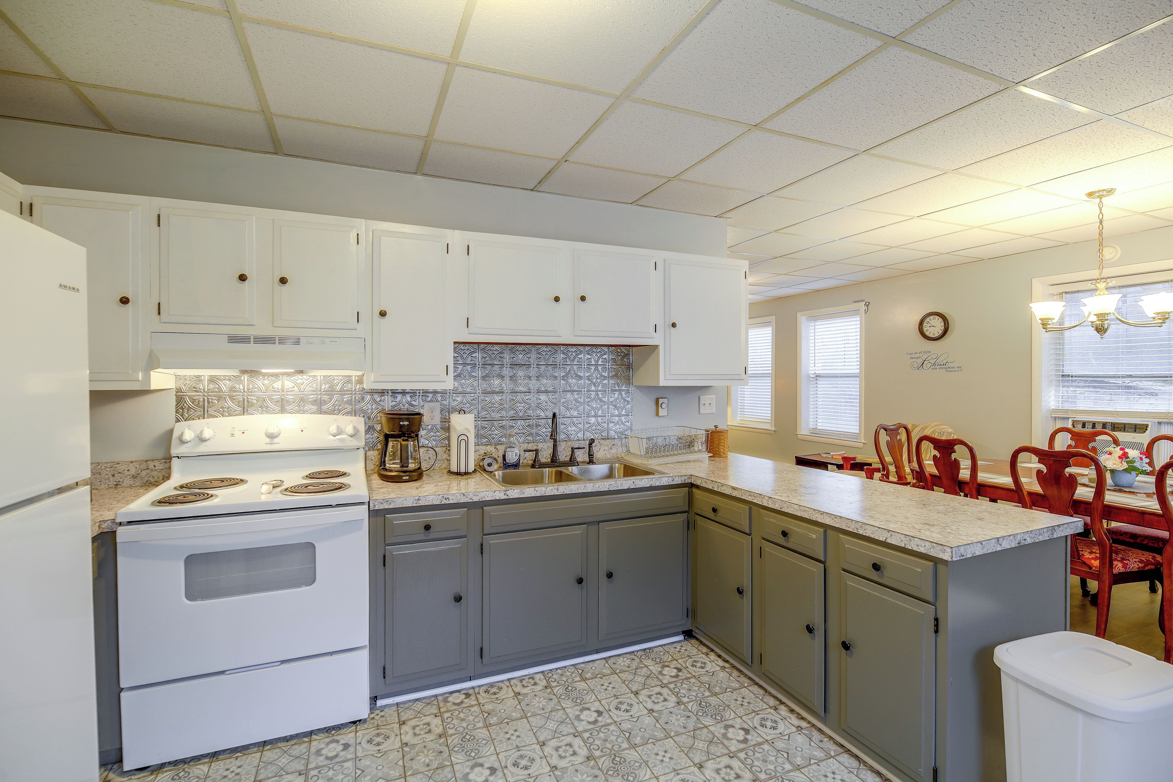 A kitchen with white cabinets, a stove, a sink, and a dining area with chairs.
