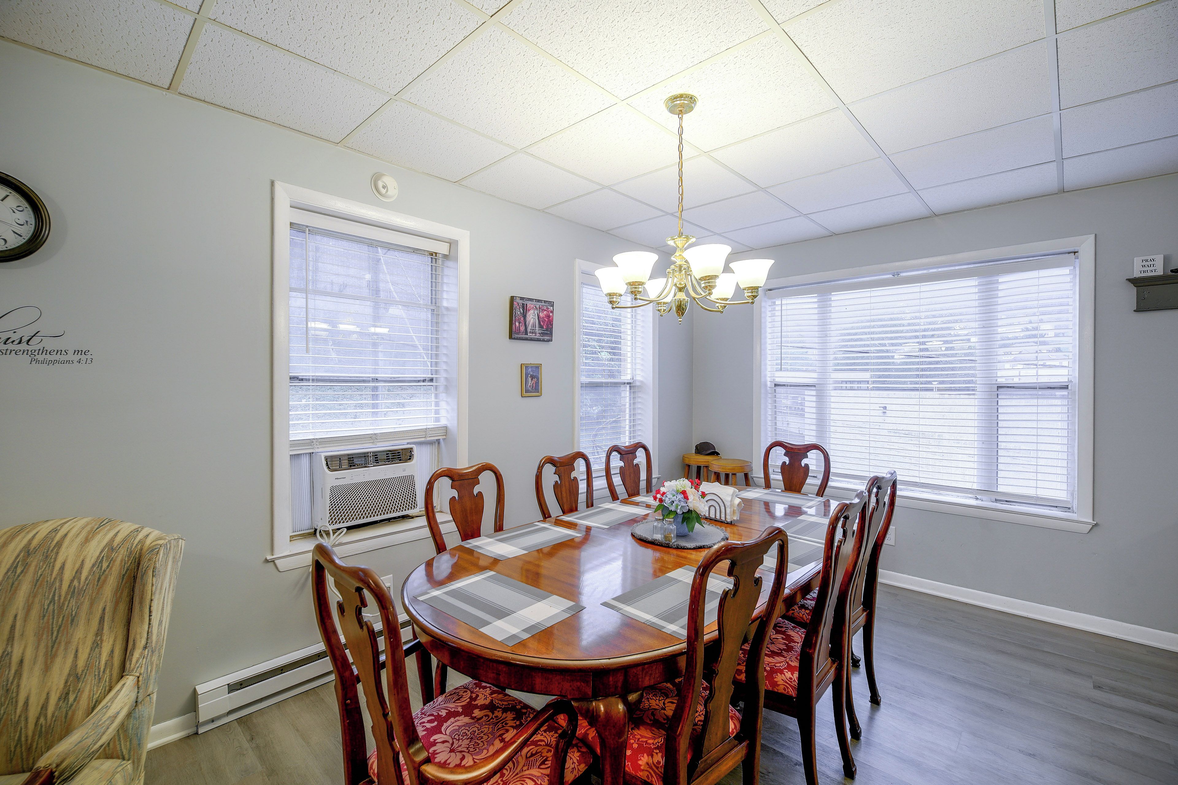 A dining room with a round table, chairs, a chandelier, and windows with blinds.