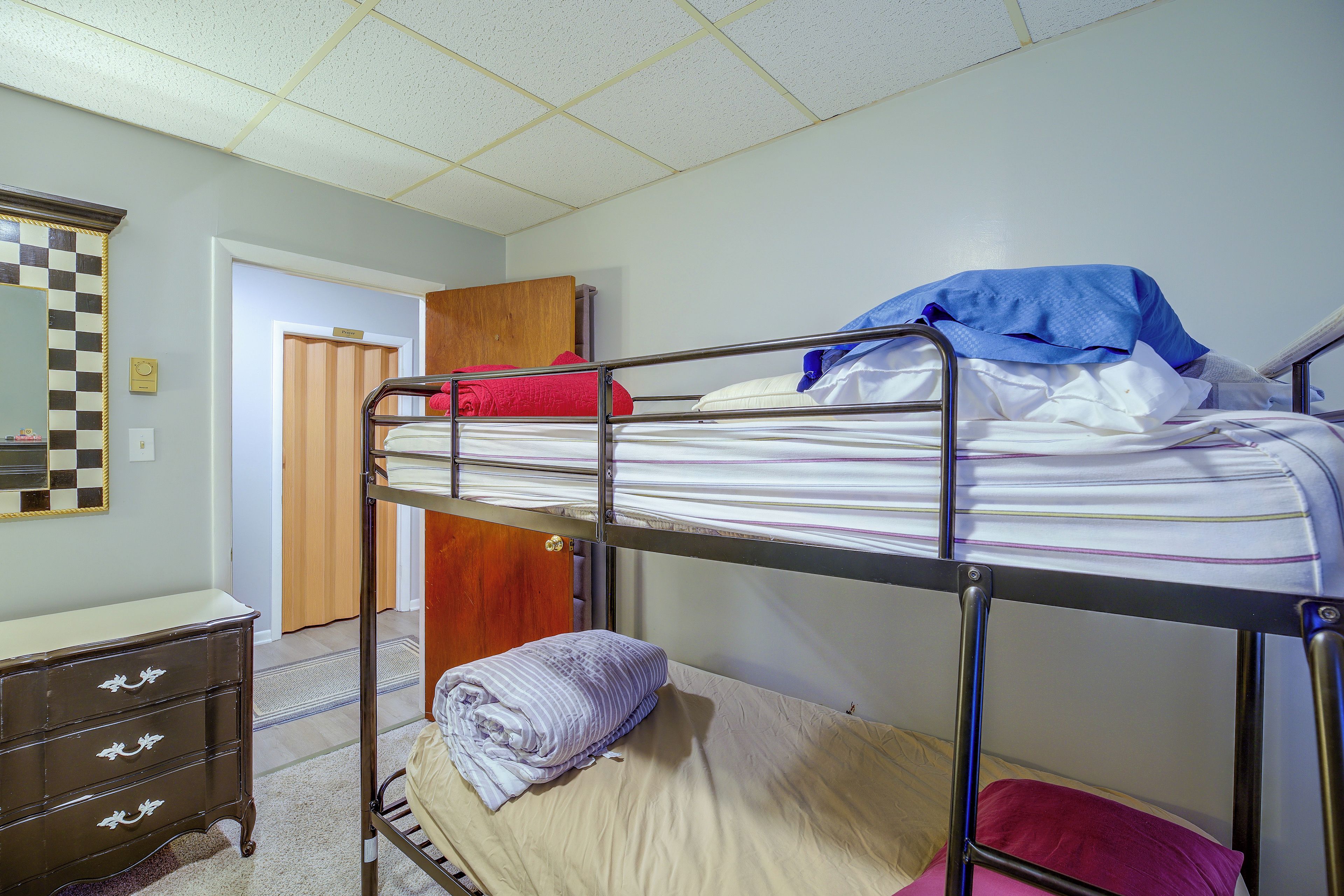 A bunk bed with a wooden headboard, a dresser with drawers, and a checkered mirror on the wall.