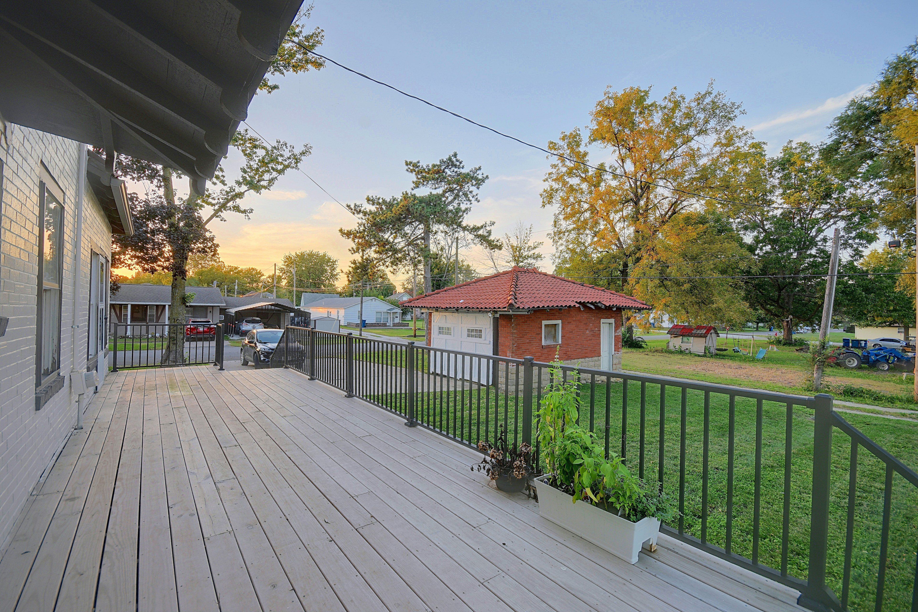 A wooden deck with a metal railing, a small shed, and a red-roofed building in the background.