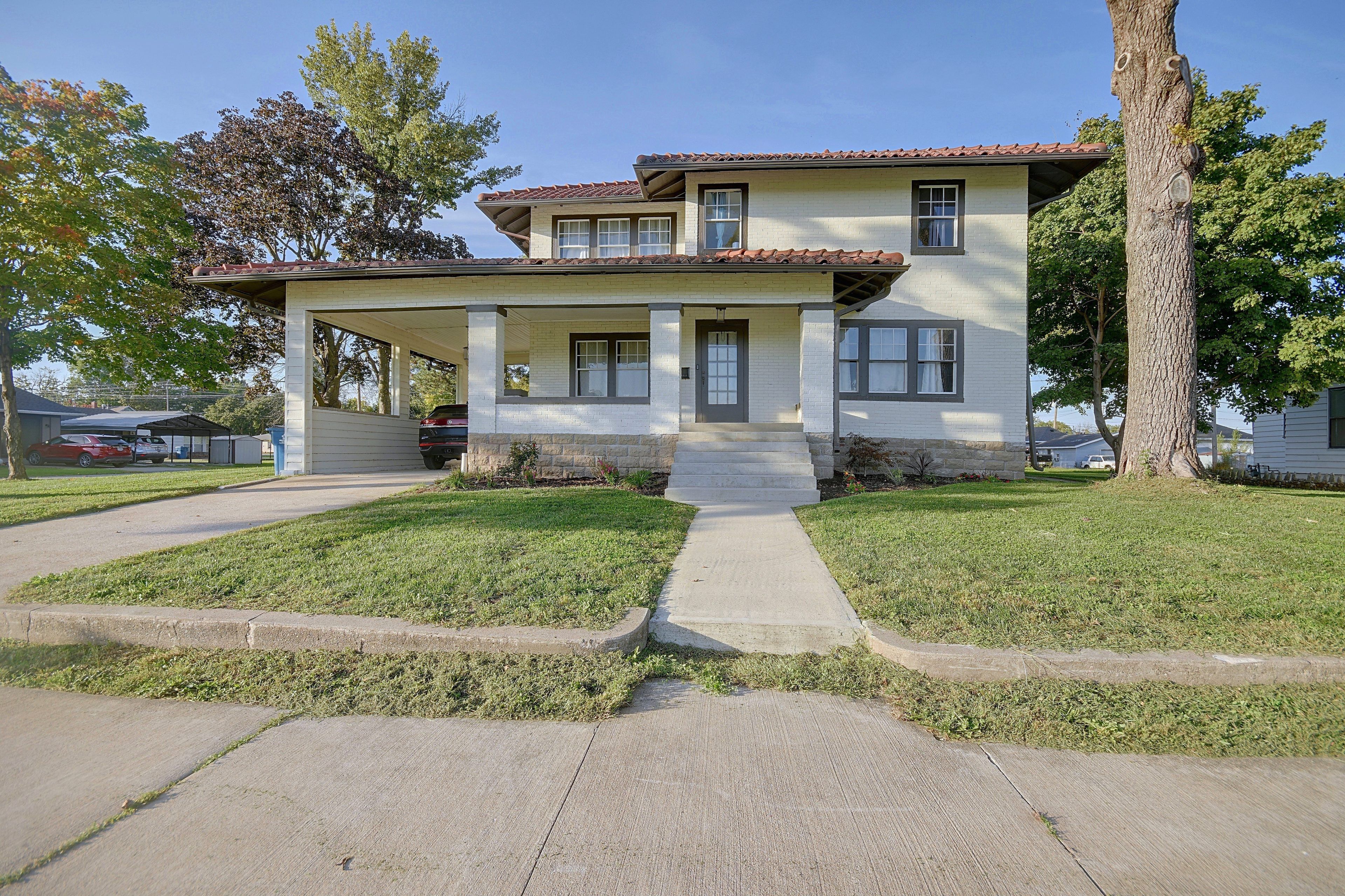 A two-story house with a covered porch, a front yard with grass, and a driveway.