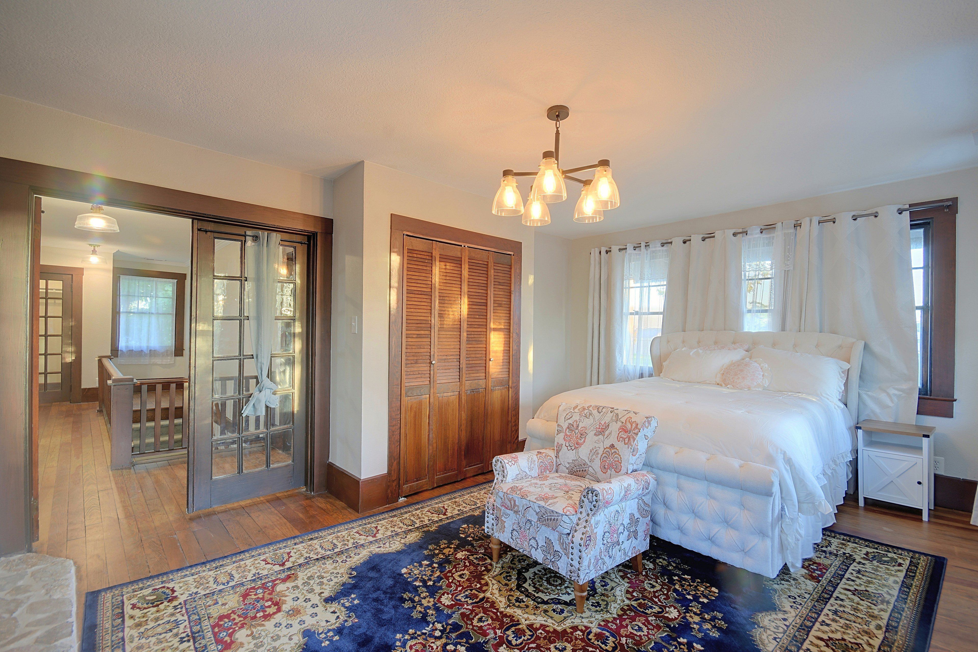 A bedroom with a large bed, a chair, a wardrobe, and a mirror.