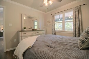 Un dormitorio con cama, cómoda, espejo, ventana con cortinas y ventilador de techo.
