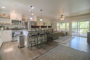 A modern kitchen with stainless steel appliances, a bar area with stools, and a large sliding glass door leading to a deck. - Eucha Home: Grand Lake Views, Boat Ramp Access (Eucha)