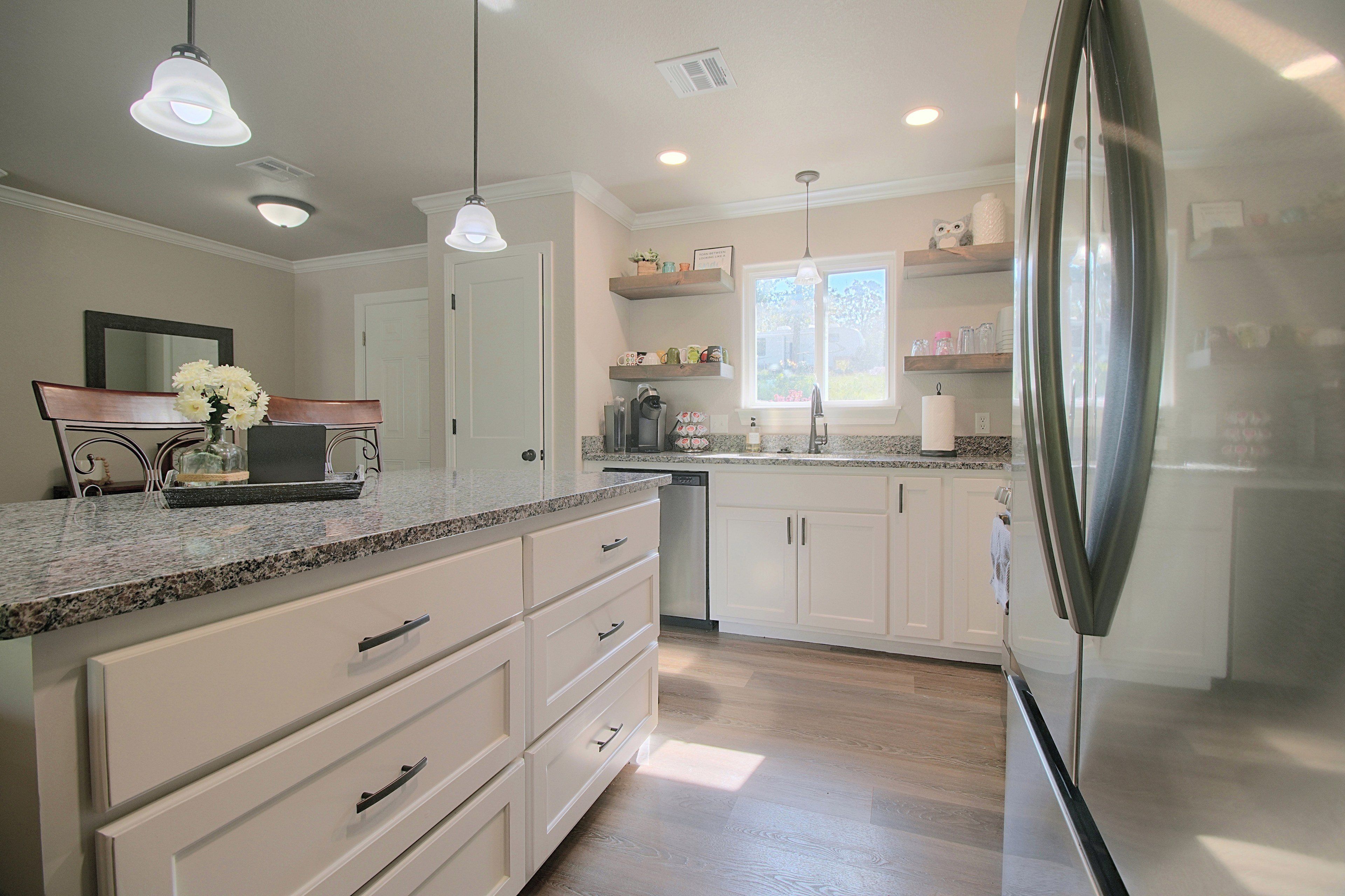 A modern kitchen with white cabinets, granite countertops, a stainless steel refrigerator, and pendant lighting.