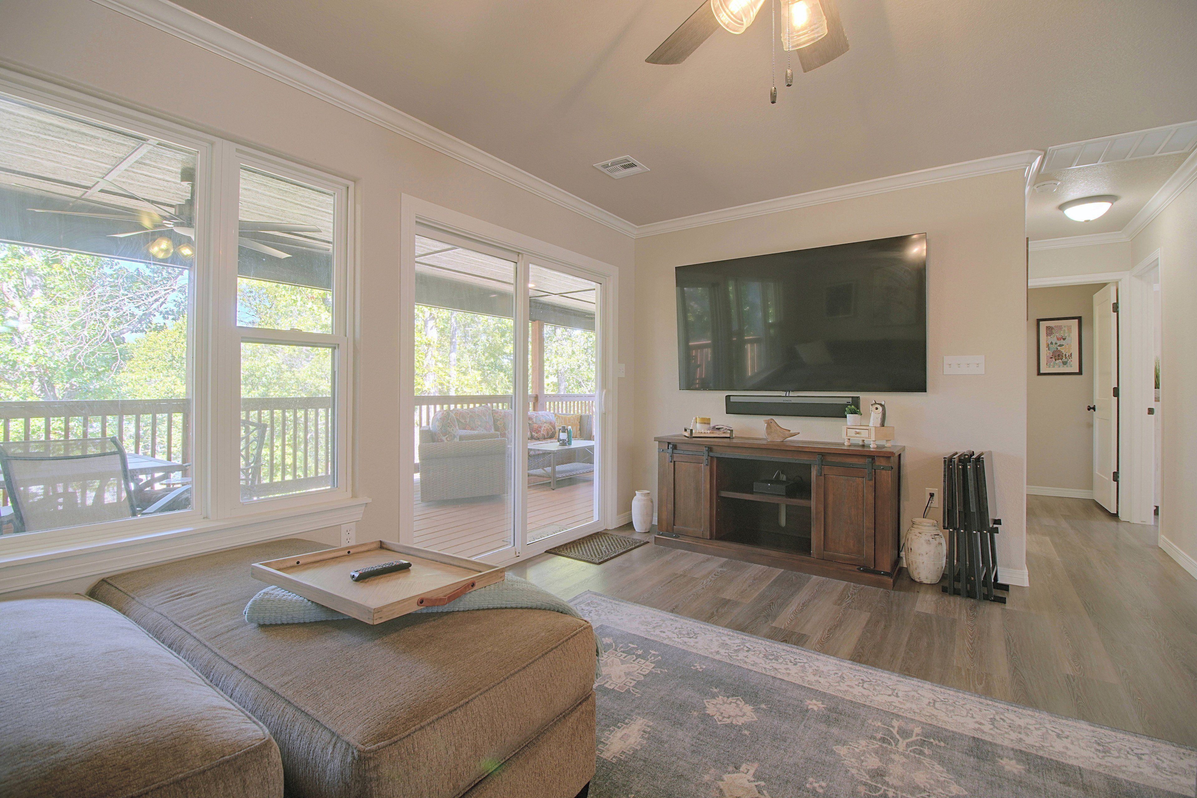 A spacious living room with a large flat-screen TV mounted on the wall, a sliding glass door leading to an outdoor area, and a cozy seating arrangement.