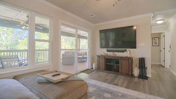 A spacious living room with a large flat-screen TV mounted on the wall, a sliding glass door leading to an outdoor area, and a cozy seating arrangement.