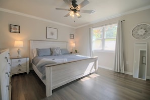 Un dormitorio con cama, mesitas de noche, ventilador de techo y ventana con cortinas.