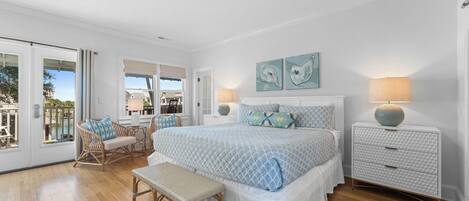 A bedroom with a large bed, a bench, a chair, a nightstand, and a view of the outdoors.