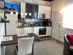 A modern kitchen with a dining area, including a TV, cabinets, and a coffee machine. - South Beach Room (Wyk auf Foehr)