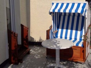 Een klein terras met een witte tafel en een blauw-wit gestreepte stoel.