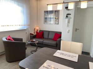 Een moderne woonkamer met een grijze bank, rode kussens, een klein bijzettafeltje en een salontafel met naambordjes.