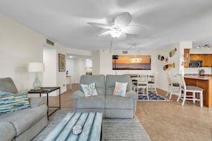 A living room with a gray sofa, a coffee table, and a dining area with a white table and chairs. - Water Views/Pool - Bahia Shores O-503 - Sunrise on the Bay (St. Petersburg)