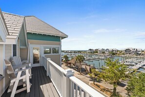 Une propriété située en bord de mer, dotée d’une terrasse, de chaises et offrant une vue sur une marina remplie de bateaux.