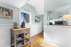 Une cuisine équipée d’un four à micro-ondes, d’un grille-pain et d’une machine à café sur le plan de travail, d’un meuble contenant de la vaisselle, et offrant une vue sur un escalier menant à une autre pièce.