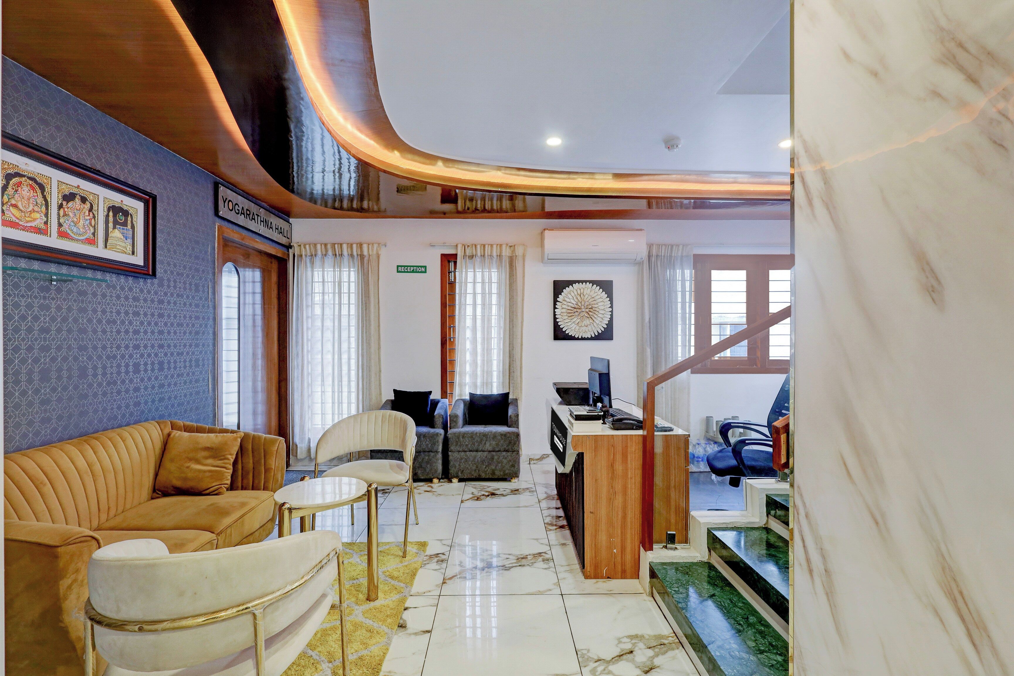 A hotel lobby with a reception desk, seating area, and a staircase leading to an upper level.