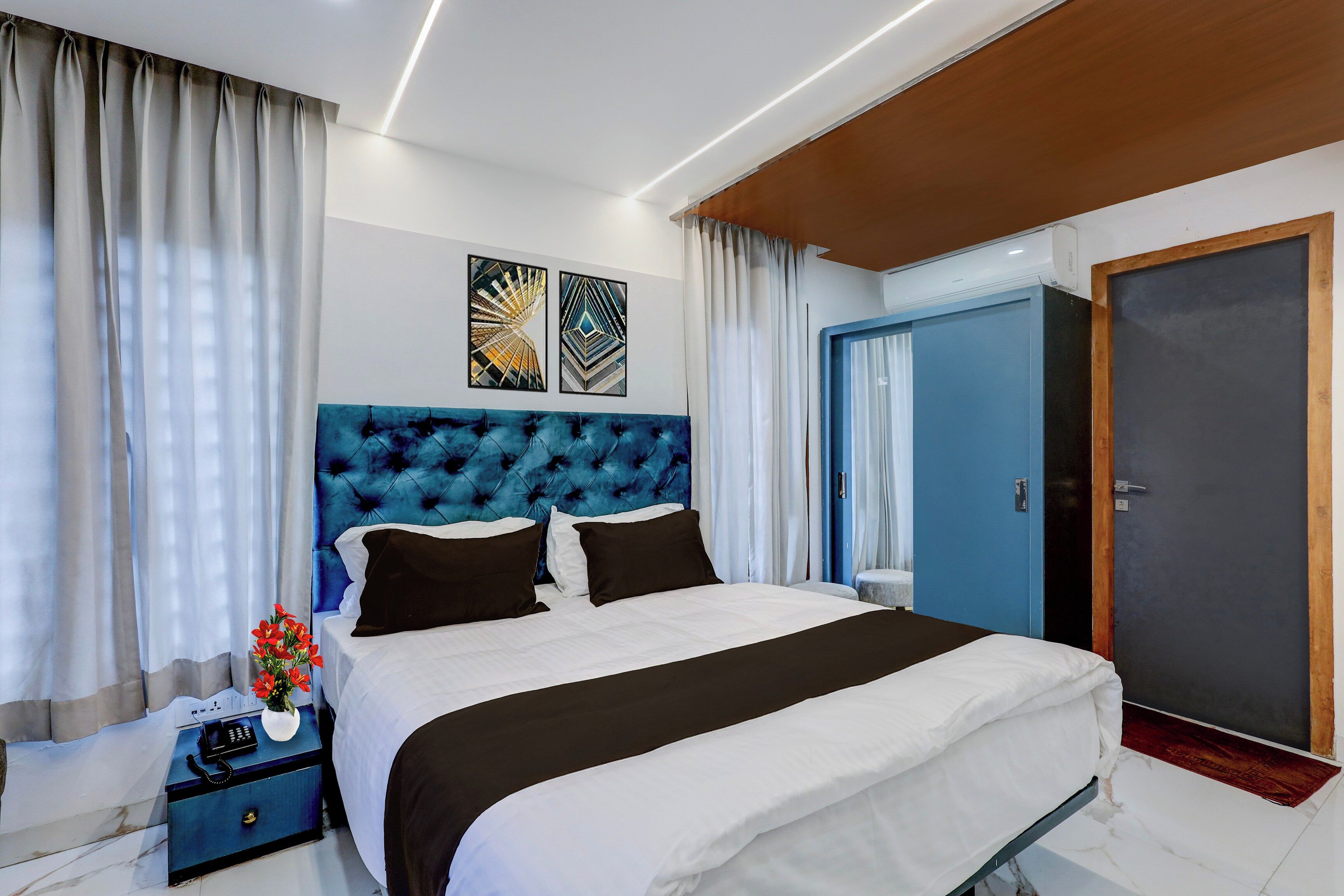 Un dormitorio moderno con una cama grande, un cabecero azul y una mesita de noche con un jarrón de flores.